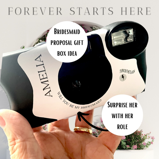 A Kodak FunSaver disposable camera with a personalised sticker for your bridesmaid or maid or honour gift box.  Shown in a hand with flowers in the background